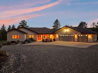 Experience luxury living in this stunning stucco home, nestled amidst mature pine trees and bathed in the warm glow of twilight.