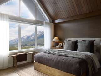 Experience breathtaking mountain views from this luxurious bedroom, featuring a vaulted wood-paneled ceiling and expansive windows.