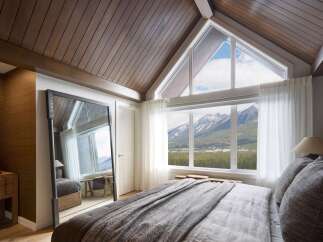 Experience breathtaking mountain views from this stunning bedroom, featuring a vaulted wood-paneled ceiling and expansive windows.