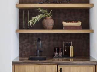 This stylish wet bar features a modern black faucet over a sleek sink, complemented by a rich, textured backsplash.