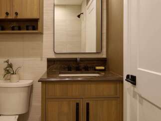 This modern bathroom features a sleek wooden vanity with dark hardware, complemented by a granite countertop and a rectangular undermount sink.