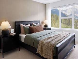Experience breathtaking mountain views from this serene bedroom, featuring a luxurious dark wood bed and plush carpeting.