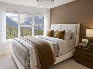 Experience breathtaking mountain views from this serene bedroom, featuring a comfortable bed dressed in neutral tones and a cozy throw.