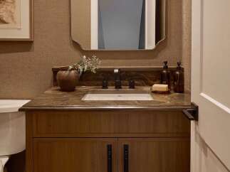 This powder room features a warm and inviting atmosphere with its textured wallpaper and rich wood vanity.