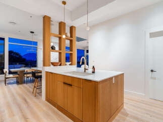 Experience modern living in this stunning open-concept kitchen and dining area, featuring a sleek island with a waterfall countertop and a chic brass faucet.