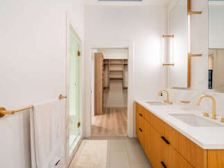 Experience modern luxury in this stunning bathroom featuring a sleek wooden vanity with dual sinks and elegant gold fixtures.