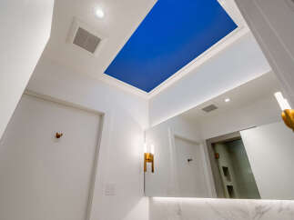 Experience modern luxury in this bathroom featuring a striking blue ceiling accent and elegant gold sconces.