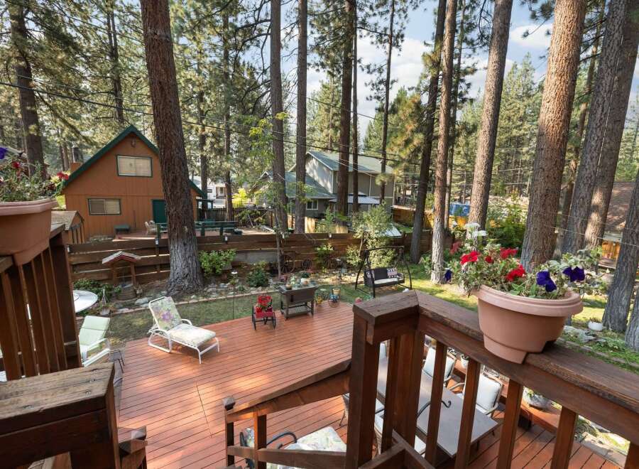 Enjoy outdoor living in this charming cabin retreat, featuring a spacious wooden deck perfect for entertaining or relaxing amidst the tall pine trees.