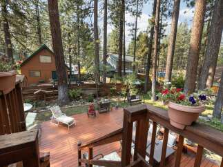 Enjoy outdoor living in this charming cabin retreat, featuring a spacious wooden deck perfect for entertaining or relaxing amidst the tall pine trees.
