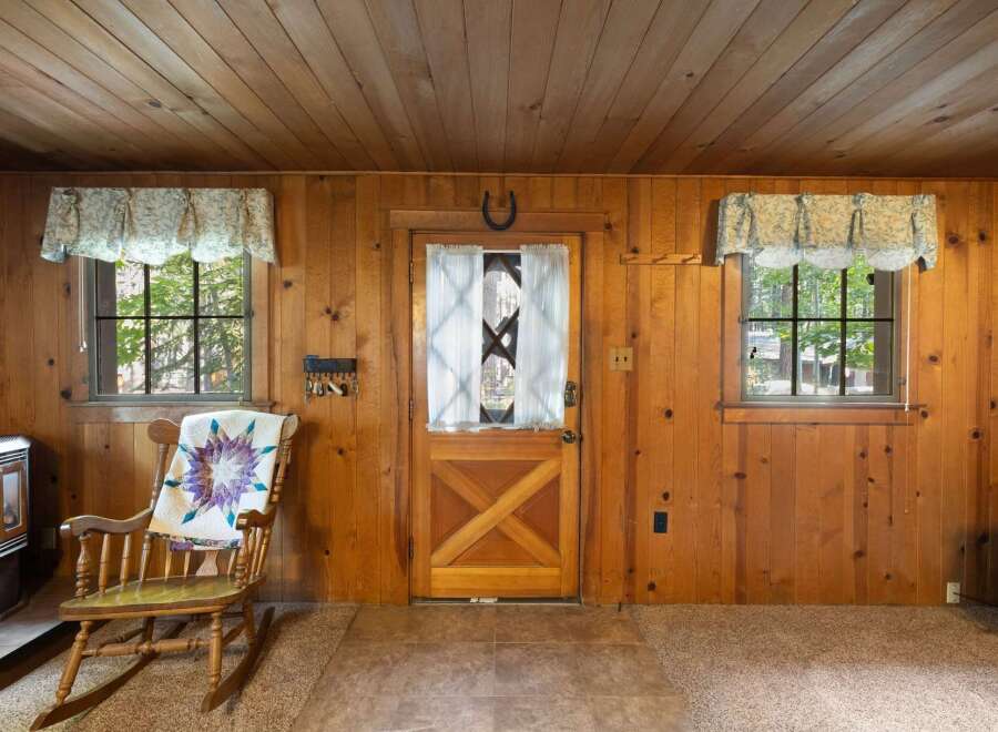 Step into a cozy cabin retreat featuring warm wood paneling throughout and a charming rocking chair adorned with a quilt.