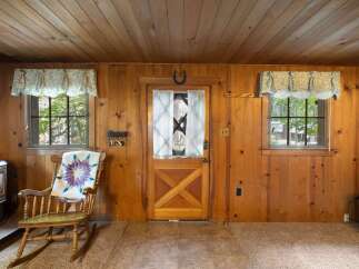 Step into a cozy cabin retreat featuring warm wood paneling throughout and a charming rocking chair adorned with a quilt.
