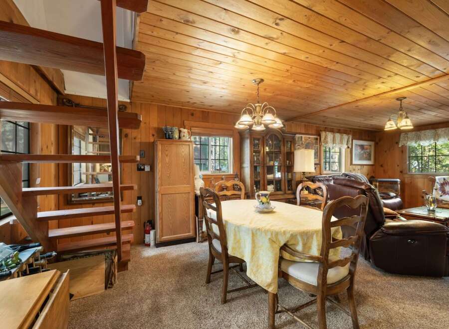 Experience rustic charm in this cozy dining and living area, featuring warm wood paneling and a charming staircase.