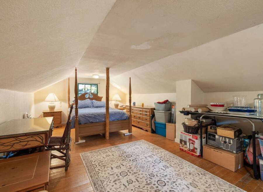 Discover this charming attic bedroom, featuring a cozy four-poster bed and a rustic wooden desk perfect for a home office setup.