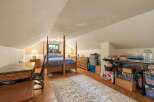 Discover this charming attic bedroom, featuring a cozy four-poster bed and a rustic wooden desk perfect for a home office setup.