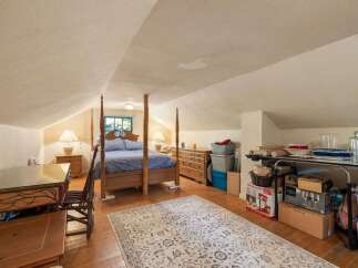 Discover this charming attic bedroom, featuring a cozy four-poster bed and a rustic wooden desk perfect for a home office setup.