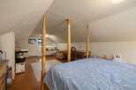 Discover this charming attic bedroom, featuring a cozy four-poster bed and a dedicated workspace with a classic wooden desk and chair.