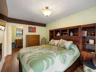 This charming bedroom features a spacious bed with a tropical-themed quilt and matching pillows, complemented by a large wooden dresser and built-in bookshelves.