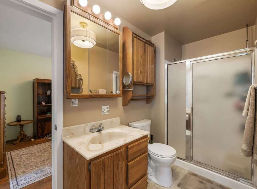 This bathroom features a wooden vanity with a marble countertop and a built-in sink, complemented by a large mirrored medicine cabinet above.