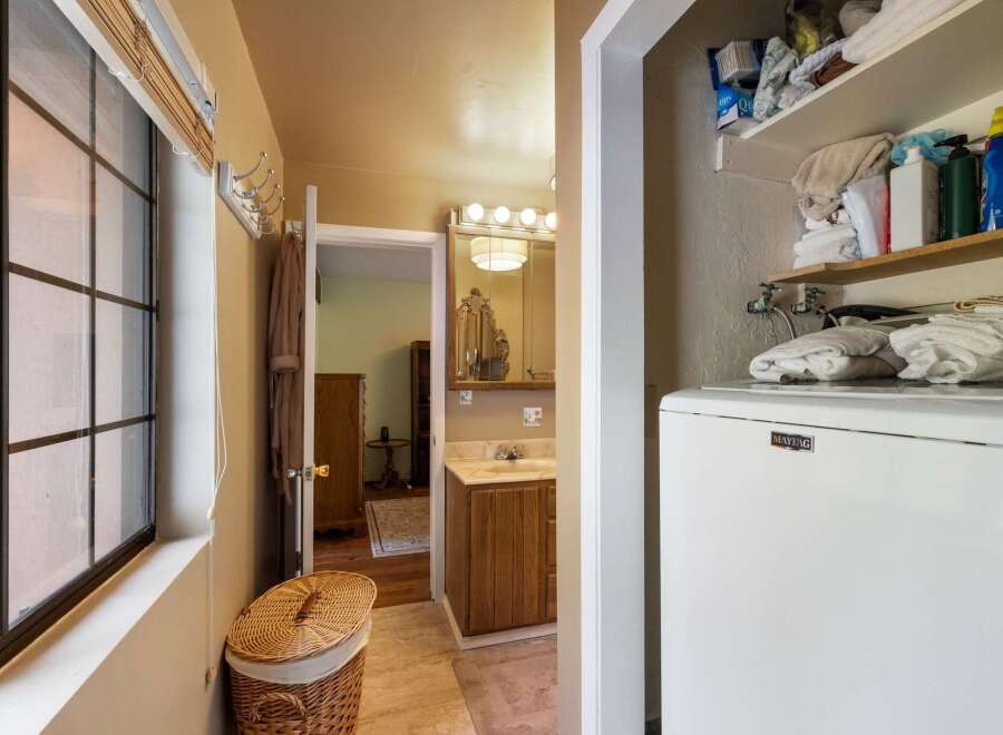 This charming bathroom features a convenient laundry area with a Maytag washer and ample storage shelves stocked with toiletries and towels.