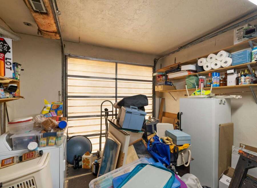 This cluttered garage space offers ample storage potential with shelves lining the walls and a large refrigerator.