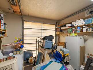 This cluttered garage space offers ample storage potential with shelves lining the walls and a large refrigerator.