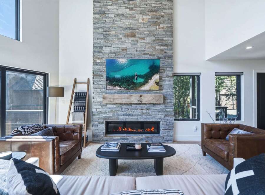 Experience modern mountain living in this stunning great room, featuring a floor-to-ceiling stone fireplace and a large flat-screen TV.