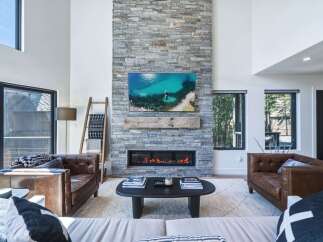 Experience modern mountain living in this stunning great room, featuring a floor-to-ceiling stone fireplace and a large flat-screen TV.