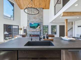 Experience luxury living in this stunning modern home featuring a grand stone fireplace and soaring vaulted ceilings with exposed wood beams.