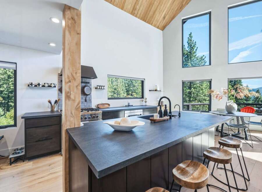 Experience modern living in this stunning kitchen featuring a large island with a waterfall countertop, sleek dark cabinetry, and a professional-grade gas range.