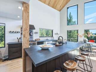 Experience modern living in this stunning kitchen featuring a large island with a waterfall countertop, sleek dark cabinetry, and a professional-grade gas range.