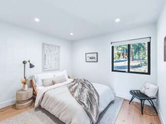 This modern bedroom features a comfortable queen-size bed with a plush throw, complemented by a stylish bedside lamp and a unique concrete side table.