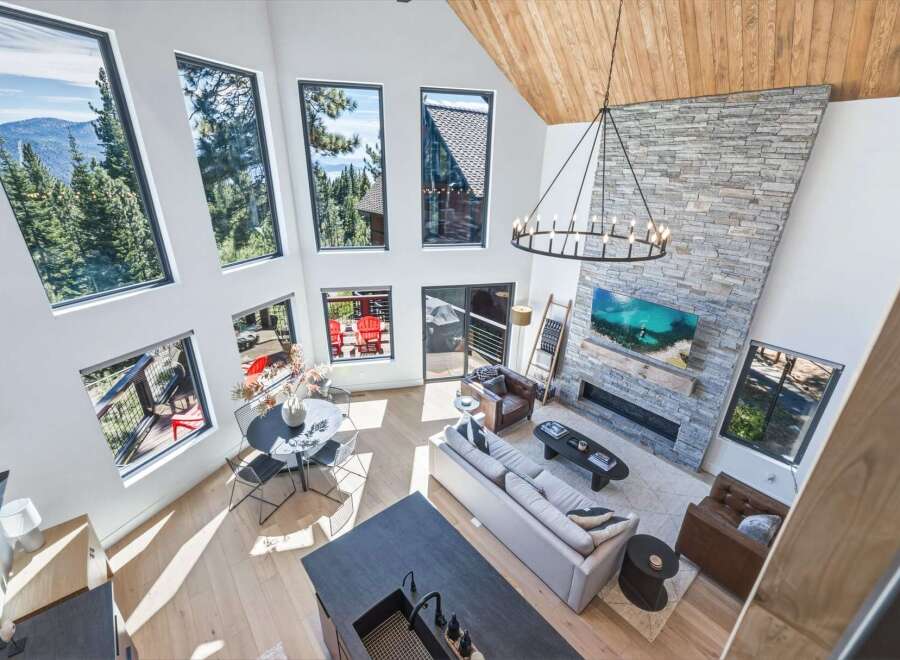 Experience breathtaking mountain views from this stunning modern living room, featuring a soaring vaulted ceiling with exposed wood beams and a dramatic floor-to-ceiling stone fireplace.