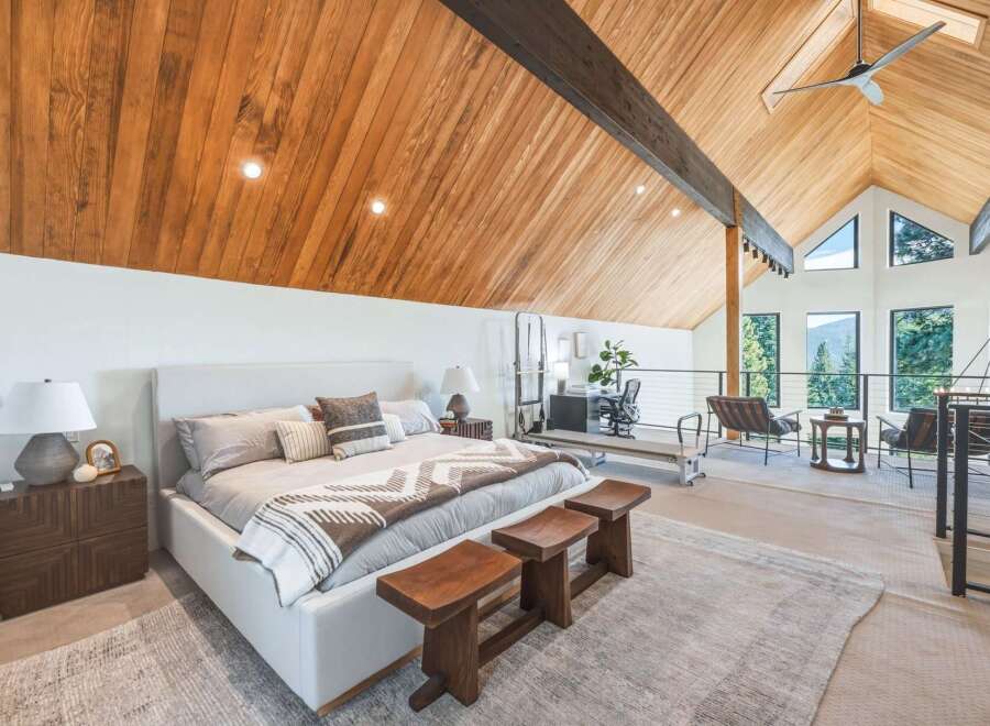 Experience luxury living in this stunning loft bedroom featuring a vaulted wood-paneled ceiling and expansive windows offering breathtaking mountain views.