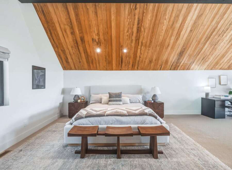 Experience modern comfort in this spacious bedroom featuring a striking wood-paneled vaulted ceiling and a plush king-sized bed.