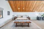 Experience modern comfort in this spacious bedroom featuring a striking wood-paneled vaulted ceiling and a plush king-sized bed.