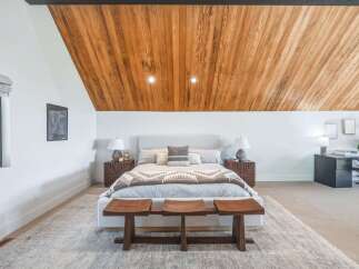Experience modern comfort in this spacious bedroom featuring a striking wood-paneled vaulted ceiling and a plush king-sized bed.