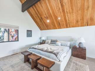 Experience rustic charm and modern comfort in this inviting bedroom, featuring a vaulted wood-paneled ceiling and a cozy king-sized bed.