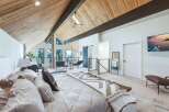 Experience luxurious mountain living in this stunning master suite, featuring a vaulted wood-paneled ceiling with exposed beams and expansive windows offering breathtaking forest views.