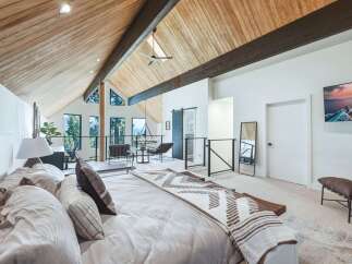 Experience luxurious mountain living in this stunning master suite, featuring a vaulted wood-paneled ceiling with exposed beams and expansive windows offering breathtaking forest views.