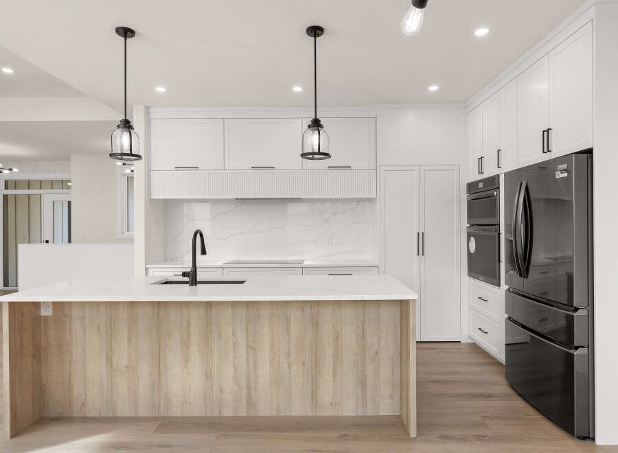 Experience modern luxury in this stunning kitchen, featuring a sleek island with a waterfall countertop and a warm wood base.