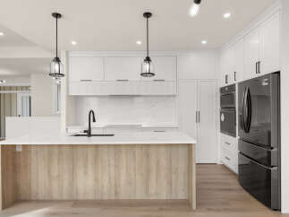 Experience modern luxury in this stunning kitchen, featuring a sleek island with a waterfall countertop and a warm wood base.
