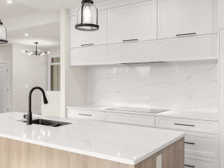 Experience modern luxury in this stunning kitchen, featuring sleek white cabinetry and a beautiful quartz countertop with a waterfall edge.