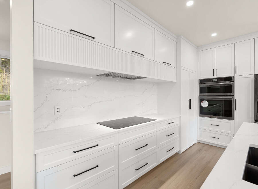 Experience modern luxury in this stunning white kitchen, featuring sleek cabinetry, a quartz backsplash, and a built-in induction cooktop.