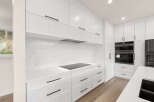Experience modern luxury in this stunning white kitchen, featuring sleek cabinetry, a quartz backsplash, and a built-in induction cooktop.