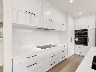 Experience modern luxury in this stunning white kitchen, featuring sleek cabinetry, a quartz backsplash, and a built-in induction cooktop.
