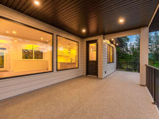 Experience luxurious indoor-outdoor living with this stunning covered patio, featuring expansive windows that offer breathtaking views of the surrounding forest.