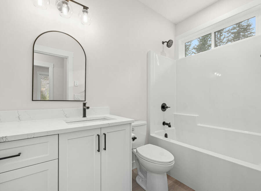 This modern bathroom features a sleek white vanity with a quartz countertop and black hardware, complemented by an arched mirror and contemporary light fixtures.