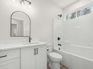 This modern bathroom features a sleek white vanity with a quartz countertop and black hardware, complemented by an arched mirror and contemporary light fixtures.