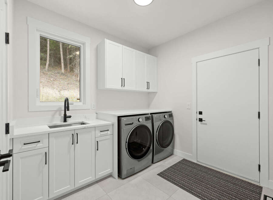 Discover this modern laundry room featuring sleek white cabinetry and a convenient undermount sink with a black faucet.