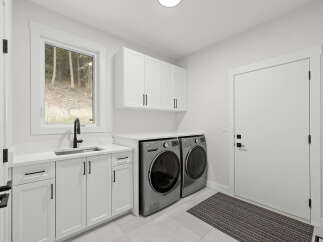 Discover this modern laundry room featuring sleek white cabinetry and a convenient undermount sink with a black faucet.